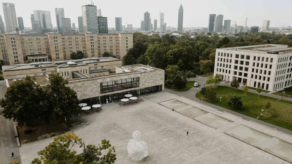 A university campus in Frankfurt, Germany, a large courtground is visible in the foreground with the tall city building visible behind it.