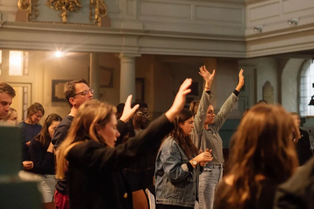 Young people gathered in an old church building. They have their hands raised and eyes closed in worship.